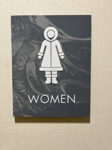 Gendered bathroom sign with figure in snowsuit at Morris Thompson Museum in Faribanks, AK