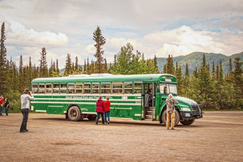 06-22-2002 Denali Alaska USA - Green transit bus in Denali National Park with tourists - one taking a picture - and evergreen trees and mountains in background