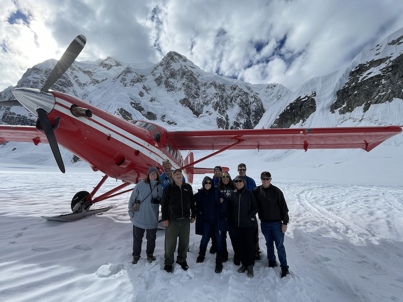 Group of eight on glacier beside red ski plane