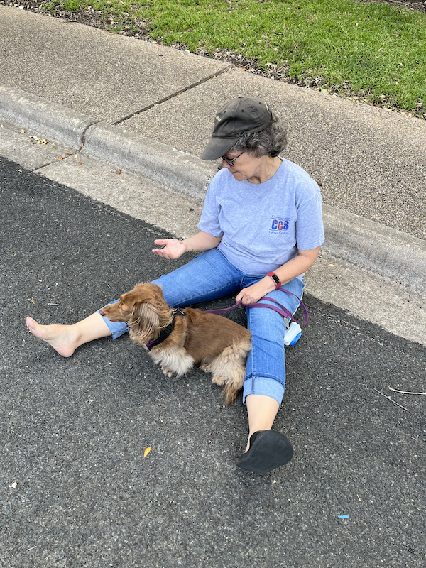 Woman with dog sitting on street next to a curb