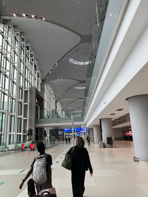 View of Susan and Sam's backs in the tall hallways in the Istanbul airport